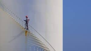 Engineer is walking up spiral staircase to working on top of fuel tank with blue sky background