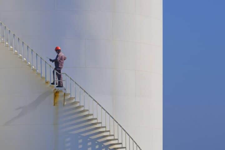 Engineer is walking up spiral staircase to working on top of fuel tank with blue sky background