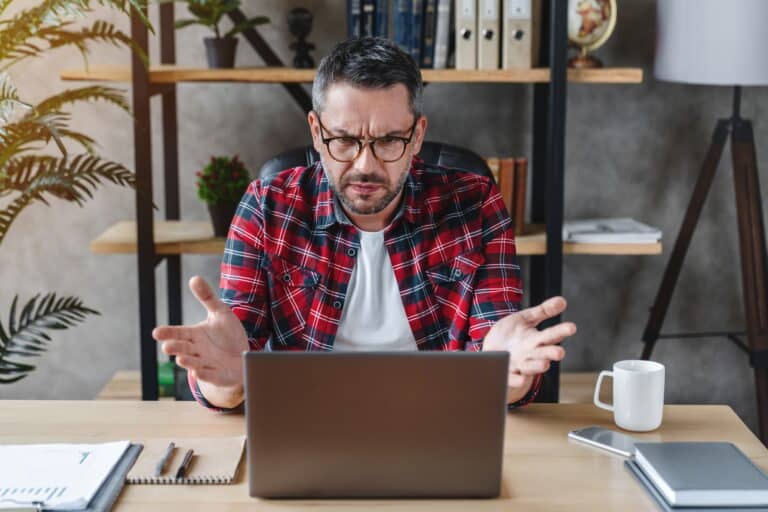 Frustrated man sitting at the desk in home office using computer