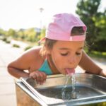 Cute thirsty girl drinks water from drinking sink